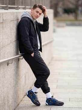 A grey hooded sweatshirt worn under a black windbreaker with nylon track pants to embrace a full athletic aesthetic.