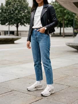 Mid-wash straight-leg jeans with a raw hem, a vintage-inspired oversized white graphic t-shirt tucked in, and a sleek black leather biker jacket.