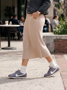 A monochromatic beige ribbed knit midi dress layered with a cropped charcoal denim jacket and finished with gold hoop earrings.