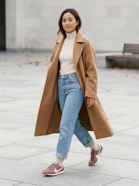 High-waisted straight-leg light wash denim jeans, a tucked-in cream ribbed turtleneck, and an oversized camel trench coat for a sophisticated autumnal look.