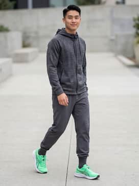 A sleek all-black athleisure set featuring charcoal grey performance joggers and a fitted black moisture-wicking zip-up hoodie to let the bright mint shoes stand out as a focal point.