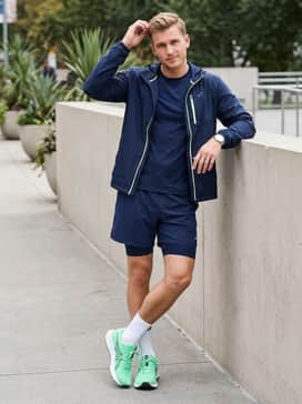 Navy blue training shorts and a matching compression shirt, layered with a neon-accented windbreaker that picks up the green tones of the sneakers for a coordinated gym look.