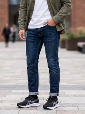 A casual weekend outfit consisting of slim-fit dark wash denim, a crisp white crew-neck t-shirt, and an unbuttoned olive green utility shirt for a rugged yet clean aesthetic.