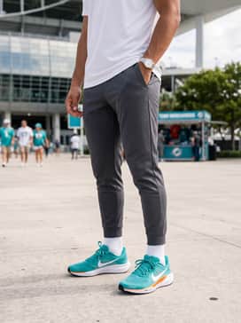 A game-day casual ensemble consisting of a white graphic team t-shirt, slim-fit tapered joggers in charcoal, and a matching aqua-colored baseball cap.