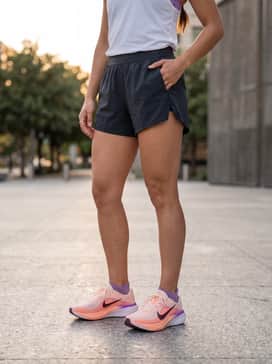 A coordinated track look featuring black 3-inch split running shorts, a lightweight white moisture-wicking tee, and a matching purple sports bra for visibility and breathability.