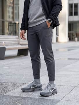 A techwear-inspired outfit consisting of tapered black technical joggers with utility pockets, a heather grey oversized hoodie, and a matte black windbreaker jacket.