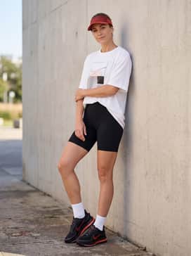 Pegasus Premium – Black high-waisted biker shorts worn with an oversized white graphic performance tee and a red tinted sports visor for a coordinated look.