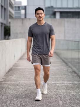 A charcoal grey moisture-wicking technical t-shirt paired with 5-inch split running shorts in a matching neutral tone and low-cut white compression socks.