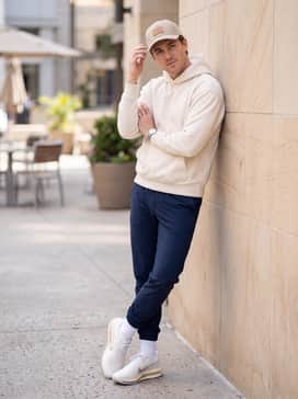 A cream-colored oversized hoodie that matches the shoe upper, paired with slim-fit navy blue track pants and a structured baseball cap.