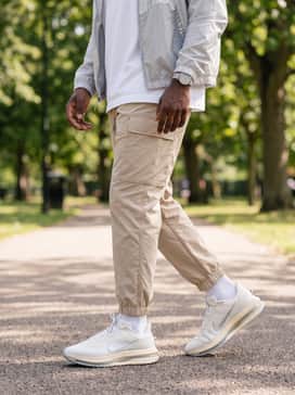 A pair of beige nylon cargo joggers with a simple white oversized tee, layered with a silver-accented windbreaker to highlight the metallic logo detail.