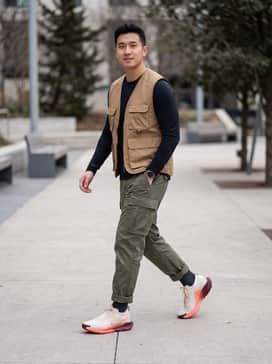 Pegasus Trail 5 Goretex – A pair of olive green water-resistant cargo pants tucked into the shoes, paired with a fitted black moisture-wicking long-sleeve base layer and a tan utility vest for a functional gorpcore aesthetic.