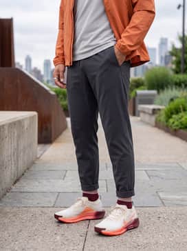 Pegasus Trail 5 Goretex – Dark charcoal grey athletic joggers with a tapered fit, combined with a light grey performance hoodie and a waterproof windbreaker in a matching orange tone to highlight the shoe's accents.