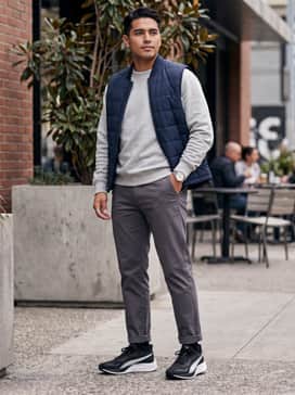 Pounce Lite – Slim-fit black chinos combined with a heather grey crewneck sweatshirt and a navy quilted vest for a smart-casual layered look.