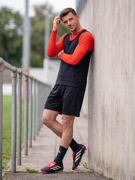 Predator Elite Foldover Tongue Soft Ground Football Boots – A high-intensity match outfit with a vibrant solar red base layer worn under a sleeveless training bib and black athletic shorts for a cohesive color-matched appearance.