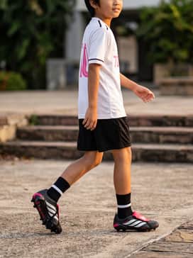 Predator League Foldover Tongue Artificial Ground Soccer Boots Kids – a complete team match kit featuring black moisture-wicking shorts and a crisp white jersey with pink numbering to match the tongue.