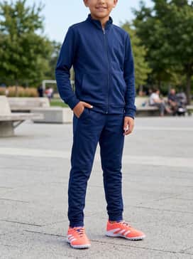 Predator League Turf Cleats Kids – A sleek navy blue tracksuit with tapered joggers and a zip-up jacket, allowing the bright coral shoes to serve as a bold statement piece.