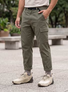 A modern streetwear aesthetic featuring slim-fit olive cargo pants, an oversized beige graphic t-shirt, and a minimalist black crossbody bag.