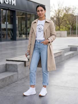 Project Rock Bsr 5 – Light-wash cropped straight-leg jeans and a tucked-in white graphic tee, layered with a beige trench coat for a sophisticated streetwear look.