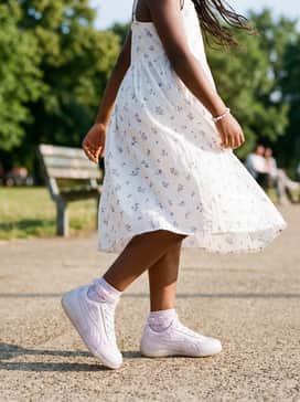 A white cotton sundress with delicate purple floral patterns and lace-trimmed ankle socks for a sweet, feminine daytime look.