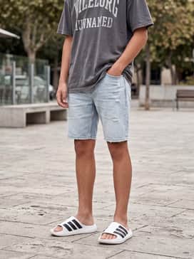 A relaxed summer outfit consisting of light-wash distressed denim shorts, an oversized charcoal grey graphic tee, and white crew socks to lean into the modern streetwear trend.