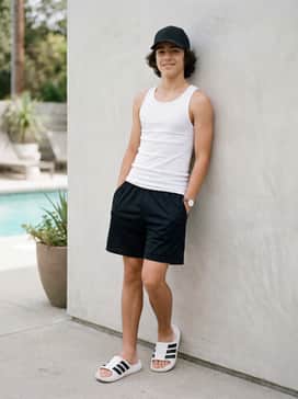 A beach-ready ensemble with black mesh athletic shorts, a bright white tank top, and a matching black baseball cap for a coordinated and functional vacation look.