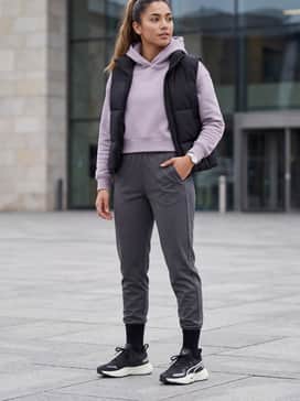 Charcoal grey tapered joggers combined with a cropped pastel hoodie and a sleek black puffer vest for a stylish post-workout ensemble.