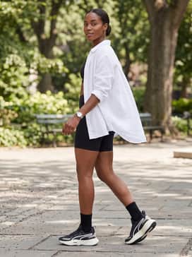 High-waisted biker shorts in a bold cobalt blue, paired with a loose-fitting white linen button-down shirt worn open over a sports bra for a summer athletic vibe.