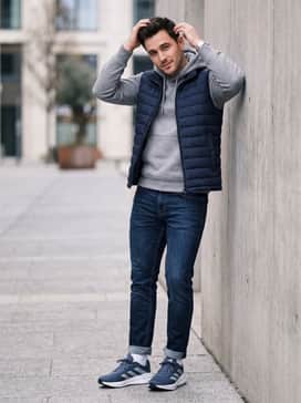 Questar 3 Running Shoes – A casual weekend ensemble consisting of dark wash slim-fit jeans, a heather grey hoodie, and a navy lightweight puffer vest.