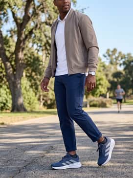 An elevated athleisure commute style with navy chinos cuffed at the ankle, a crisp white polo shirt, and a neutral-toned bomber jacket.
