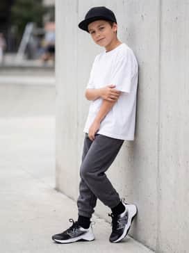 A trendy streetwear ensemble with charcoal grey fleece joggers, an oversized white graphic tee, and a black snapback cap for a cool, urban vibe.