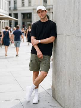 Rebound V6 Wide Mens Sneakers – An utilitarian outdoor-inspired outfit consisting of olive green cargo shorts, a black heavyweight cotton t-shirt, and a white baseball cap.