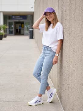 Light-wash cropped slim jeans with a tucked-in oversized white graphic tee and a purple baseball cap for a casual weekend look.