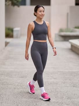High-waisted charcoal grey performance leggings paired with a matching moisture-wicking crop top and a lightweight white running gilet for a sleek, monochromatic gym look.