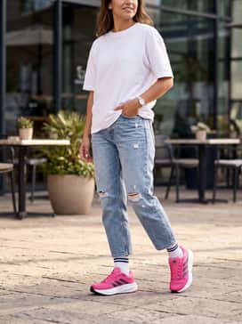 Distressed light-wash cropped jeans, a simple white oversized graphic tee tucked in, and a navy baseball cap to complement the shoe's side stripes for a relaxed weekend outing.