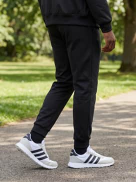 Black slim-fit tech trousers paired with a minimalist black bomber jacket and a white long-sleeve henley shirt to create a sharp, monochrome streetwear look that lets the white and grey tones of the sneakers pop.