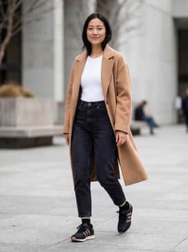 High-waisted black mom jeans paired with a tucked-in white bodysuit and an oversized camel-colored wool coat for a chic, balanced silhouette.
