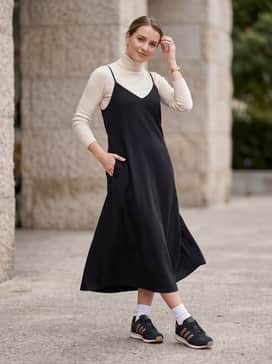 A mid-length black slip dress layered over a fitted cream turtleneck, adding a touch of feminine sophistication to the sporty footwear.