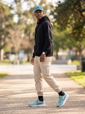 A streetwear-inspired look pairing beige cargo pants with elastic cuffs, an oversized black graphic hoodie, and a matching teal baseball cap.