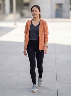 High-waisted black compression leggings paired with a charcoal moisture-wicking tank and a lightweight orange windbreaker to highlight the shoe's accents.