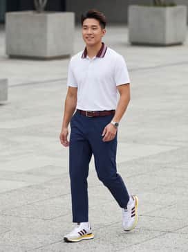 A professional golf ensemble including tailored navy tech trousers, a white performance polo, and a burgundy leather belt to echo the shoe's stripes.