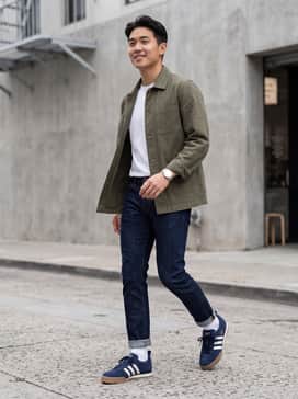 Slim-fit dark indigo jeans paired with a crisp white t-shirt and an open olive chore jacket for a rugged, timeless look.