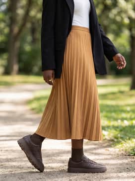 A pleated midi skirt in a tan or ochre shade, combined with an oversized black blazer and a simple white bodysuit to create a chic, high-low fashion contrast.