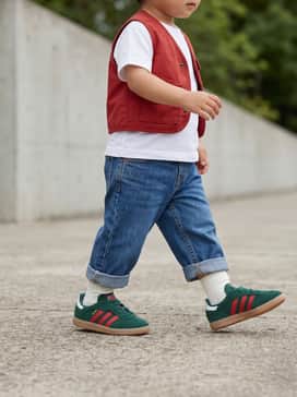 Cuffed straight-leg denim jeans paired with a crisp white crewneck tee and a small red utility vest to highlight the shoe's iconic stripes.