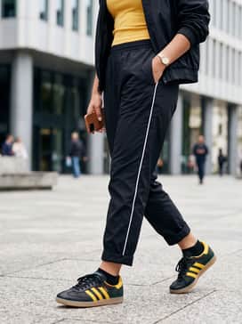 Samba Og Jamaica X Bob Marley Shoes – Black nylon track pants with a white side stripe, a tucked-in yellow ribbed tank top, and a lightweight black bomber jacket for a sporty retro aesthetic.