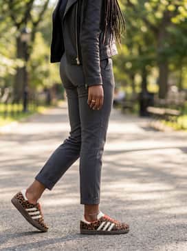 Relaxed fit charcoal grey trousers with a tucked-in black bodysuit and a leather biker jacket for a polished, high-contrast street style.