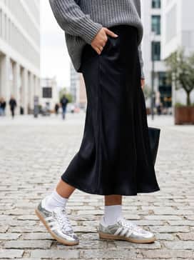 A black satin midi skirt paired with a chunky grey knit sweater for a sophisticated play on textures and a balanced, high-low fashion look.