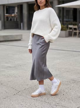 A sleek grey satin midi skirt paired with a chunky oversized white knit sweater for a soft, textural contrast that emphasizes the platform height.