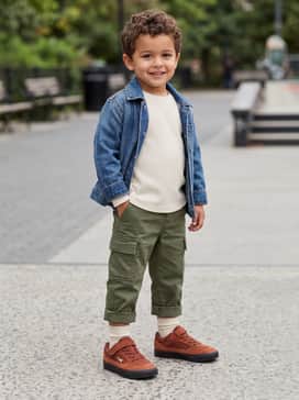 A rugged outdoor outfit consisting of olive green cargo pants, a cream-colored long-sleeve waffle knit shirt, and a durable denim jacket for cooler weather.
