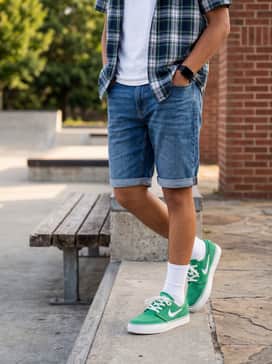Sb Stefan Janoski – Cuffed mid-wash denim shorts styled with a crisp white pocket tee and an open short-sleeve plaid shirt in navy and green tones to tie the look together.