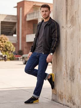 Straight-leg dark wash denim cuffed at the ankle, worn with a black polo shirt and a vintage-style racing windbreaker for a classic trackside aesthetic.